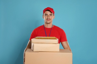 Happy young courier with parcels and envelopes on blue background