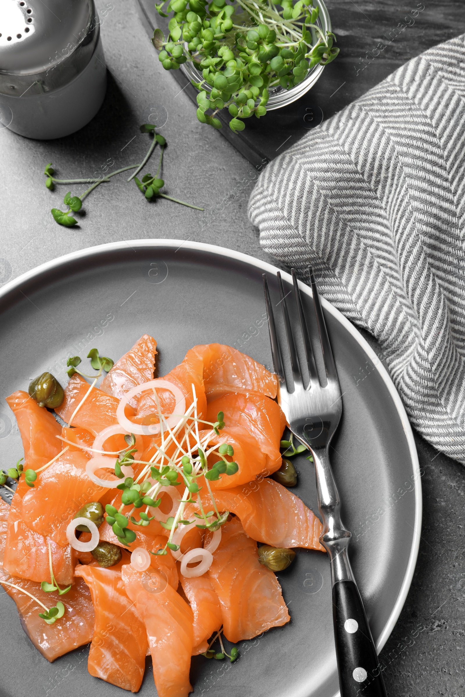 Photo of Salmon carpaccio with capers, onion and microgreens on grey table, flat lay