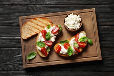 Photo of Toasted bread with tasty cream cheese and tomatoes on wooden table, flat lay