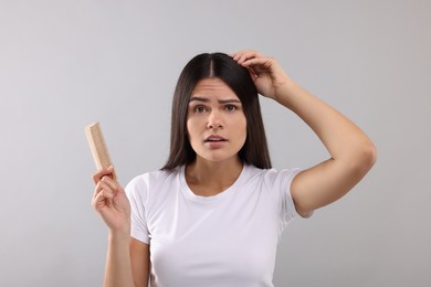 Photo of Emotional woman with comb examining her hair and scalp on grey background
