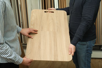 Photo of Men holding sample of wooden flooring in shop, closeup