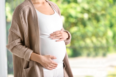 Photo of Pregnant woman standing near window at home, closeup