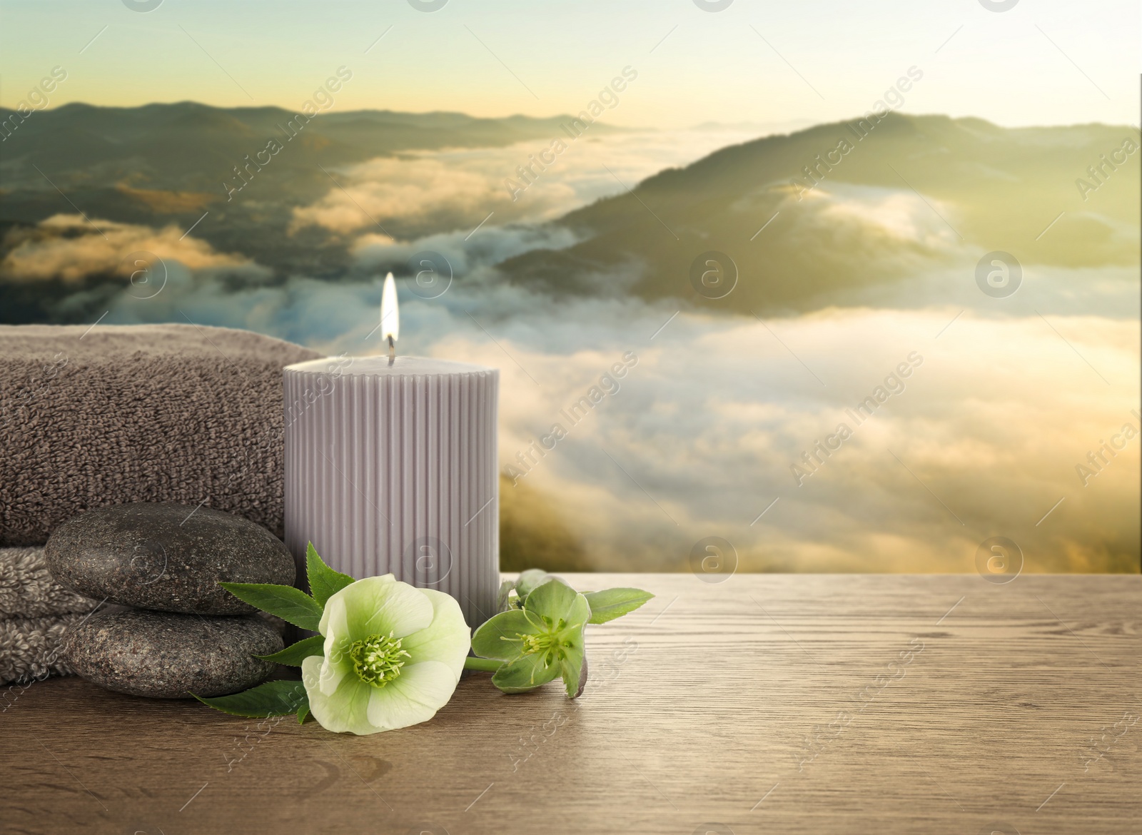 Image of Composition with spa stones and candle on wooden table against beautiful mountain landscape in morning, space for text