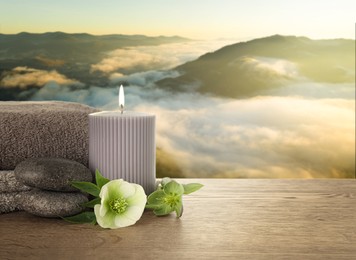 Composition with spa stones and candle on wooden table against beautiful mountain landscape in morning, space for text