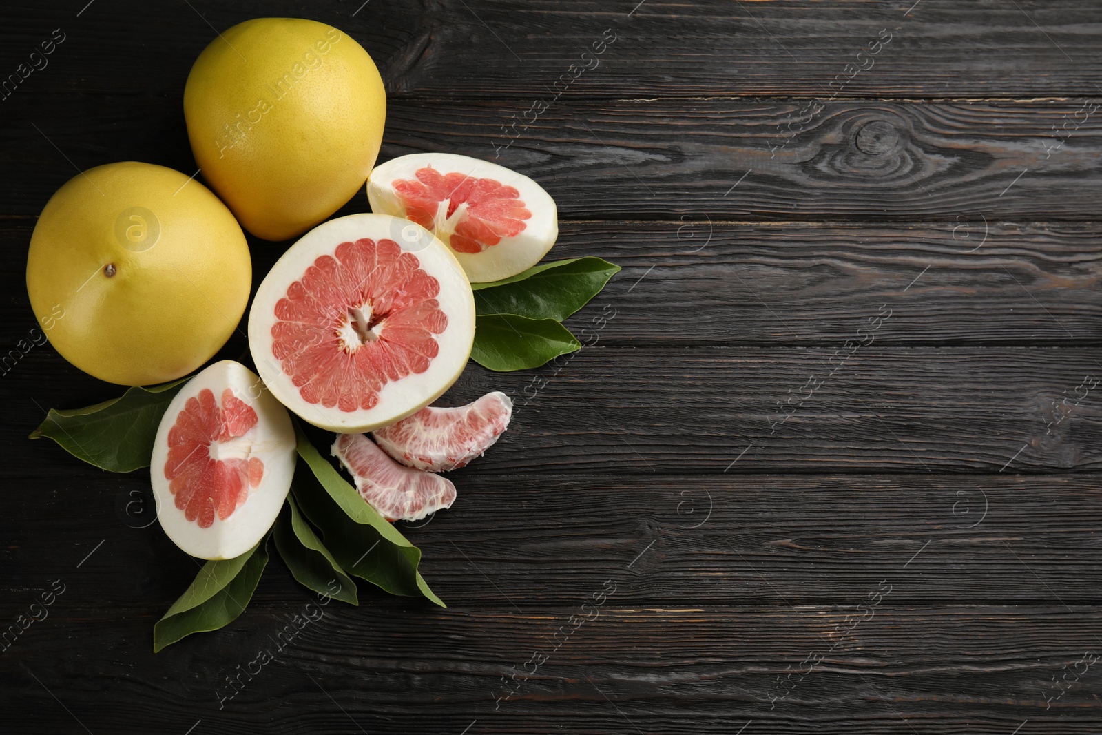 Photo of Fresh cut and whole pomelo fruits on black wooden table, flat lay. Space for text