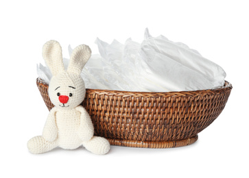 Photo of Wicker bowl with disposable diapers and toy bunny on white background