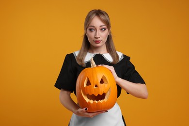 Photo of Woman in scary maid costume with carved pumpkin on orange background. Halloween celebration