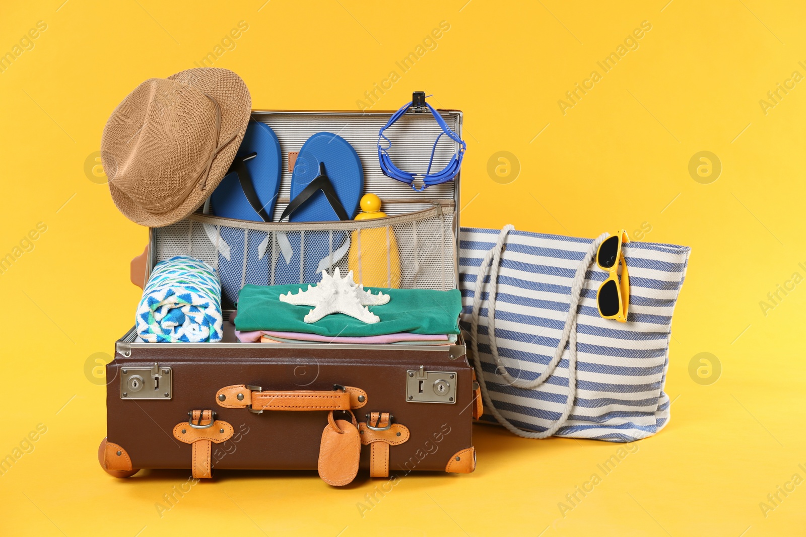 Photo of Bag and open vintage suitcase with different beach objects packed for summer vacation on orange background