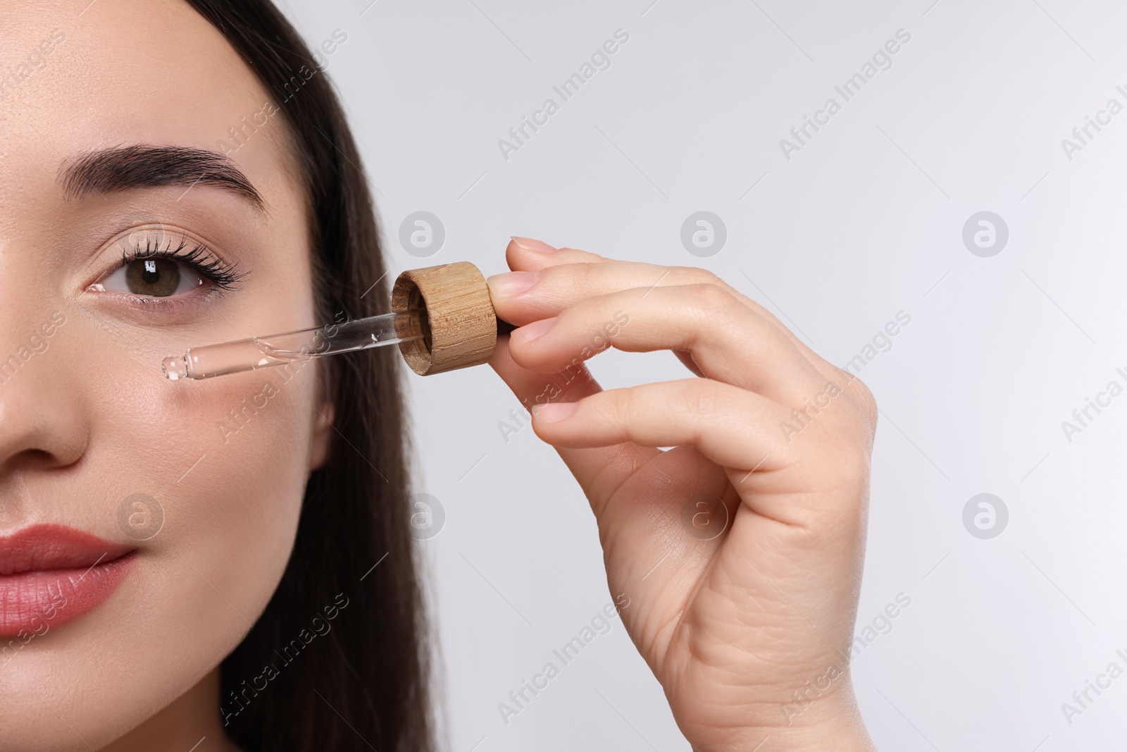 Photo of Young woman applying essential oil onto face on white background, closeup and space for text