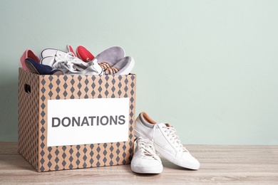 Photo of Donation box with shoes on wooden table against color background