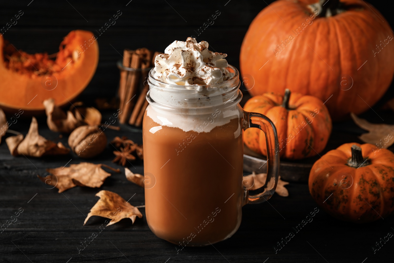 Photo of Delicious pumpkin latte on black wooden table, closeup