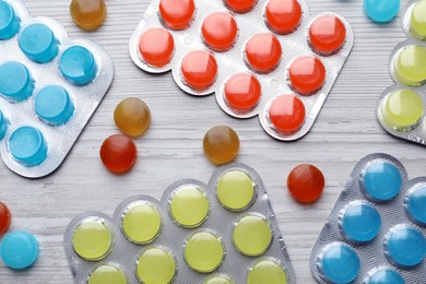 Colorful cough drops on white wooden background, flat lay