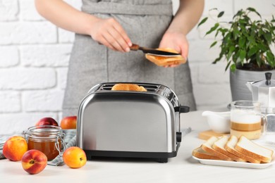 Photo of Woman spreading roasted bread with nectarine jam, closeup. Focus on modern toaster