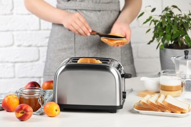 Woman spreading roasted bread with nectarine jam, closeup. Focus on modern toaster