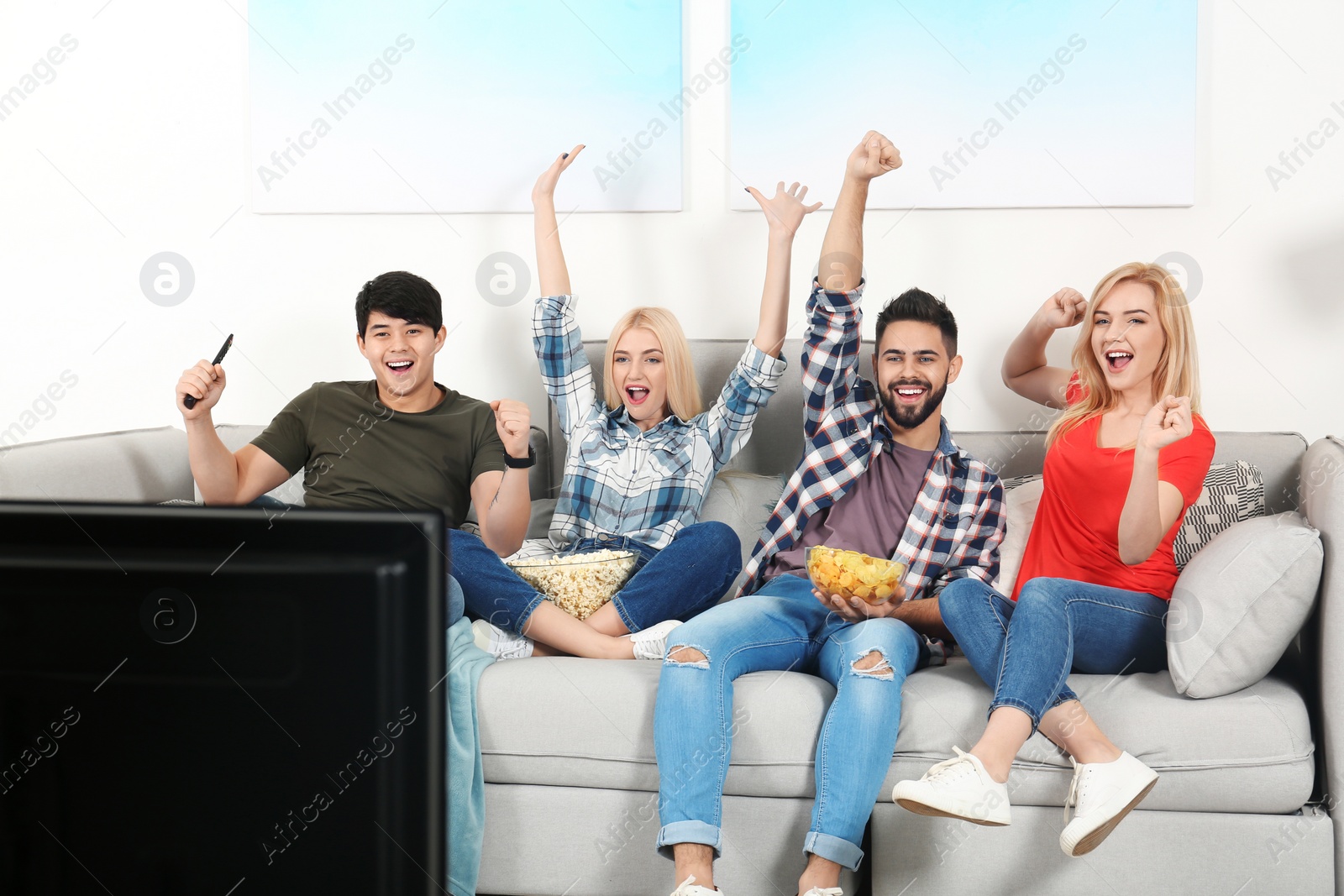 Photo of Young people with snacks watching TV on sofa at home