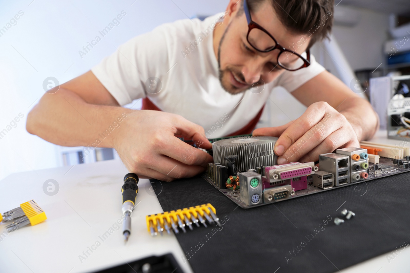 Photo of Male technician repairing motherboard at table indoors