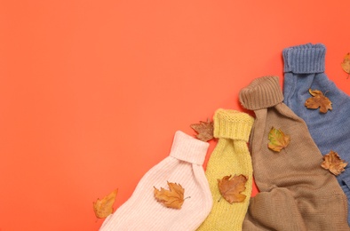 Photo of Warm sweaters and dry leaves on orange background, flat lay with space for text. Autumn season