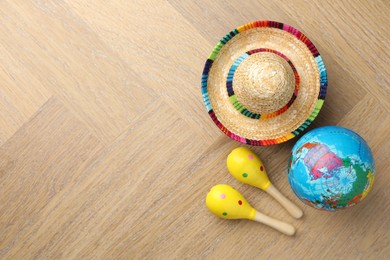 Mexican sombrero hat, globe and maracas on wooden table, flat lay. Space for text