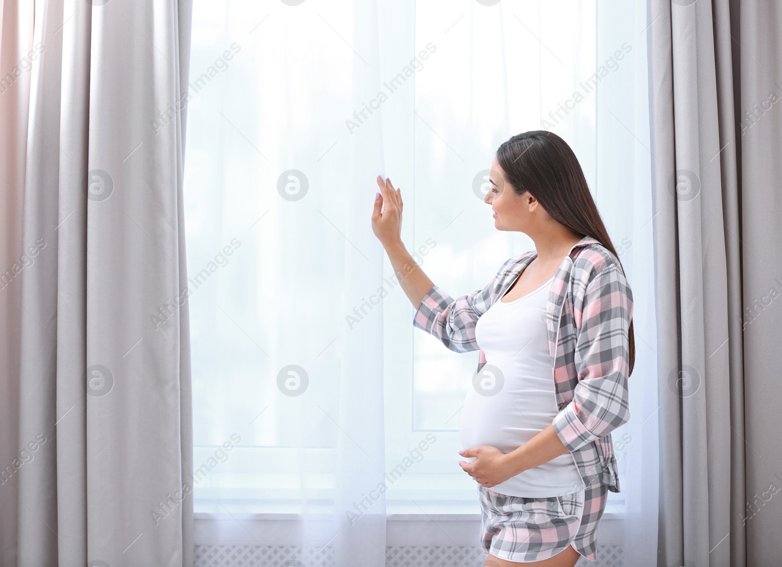 Photo of Young beautiful pregnant woman near window at home