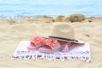 Photo of Blanket with slippers, straw hat and seashell on sand near sea. Beach accessories