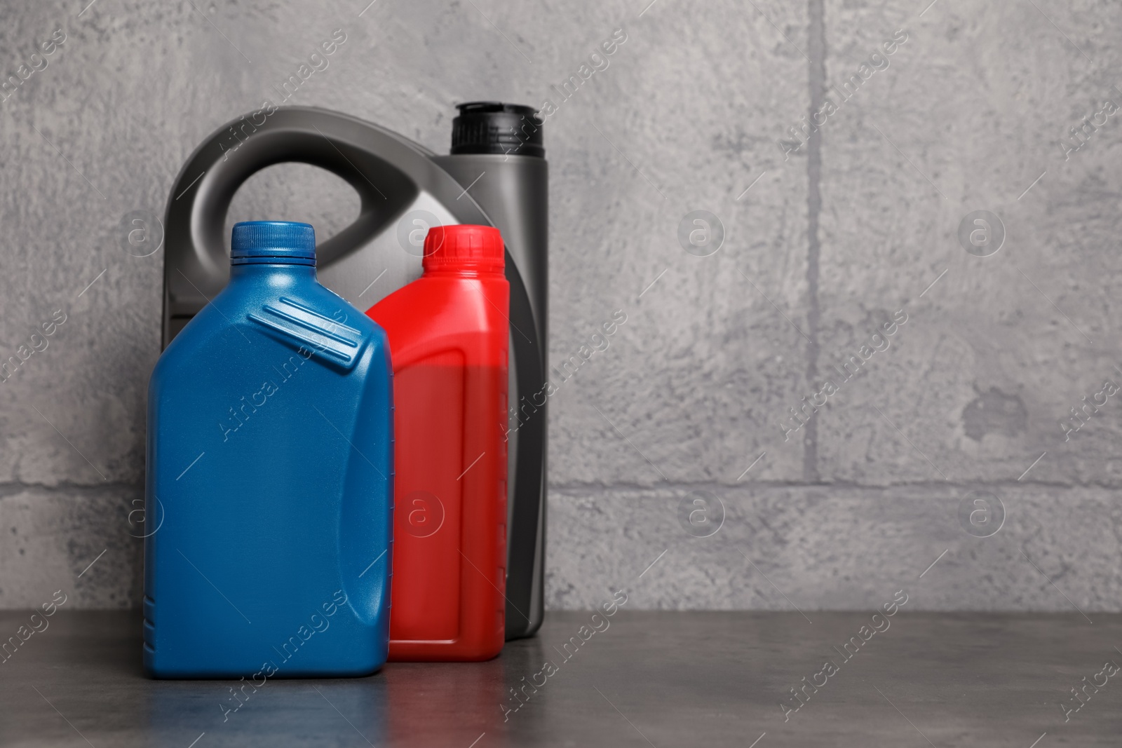 Photo of Motor oil in different canisters on table near grey wall, space for text