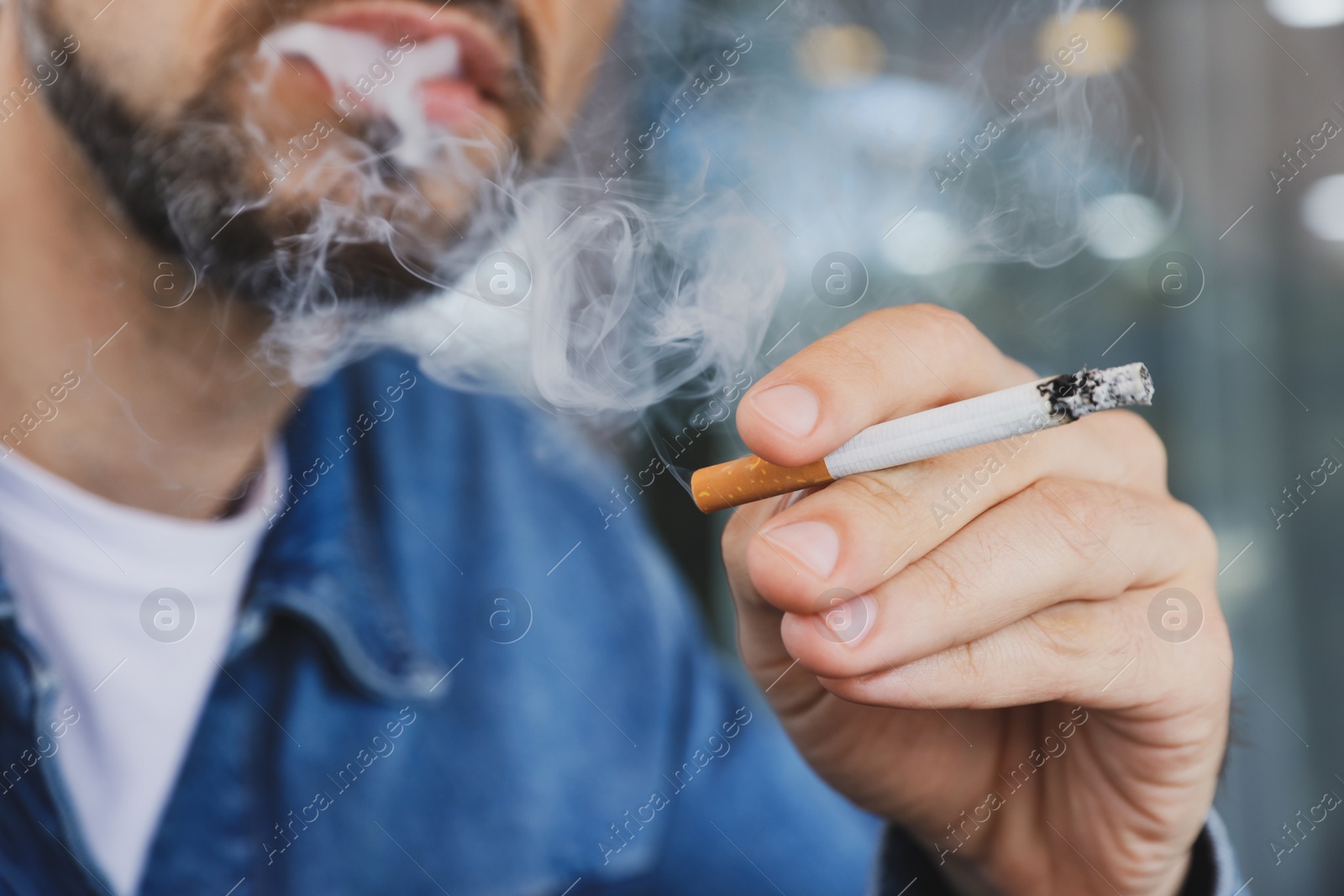 Photo of Handsome man smoking cigarette outdoors, closeup. Bad habit