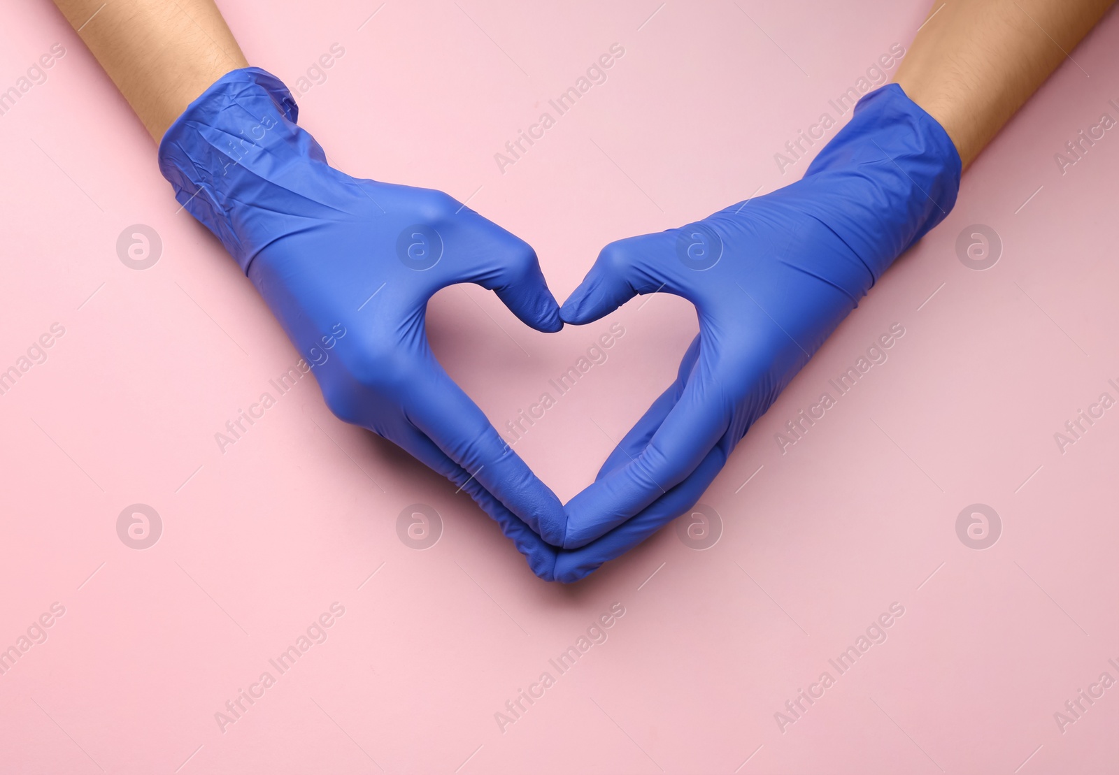 Photo of Person in medical gloves showing heart gesture against pink background, closeup of hands