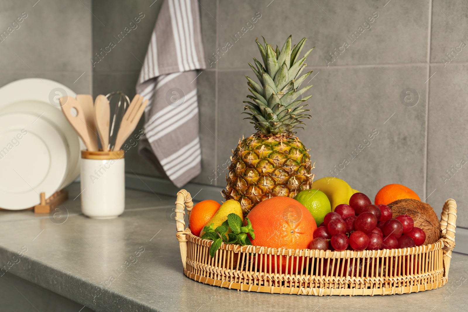 Photo of Wicker tray with different ripe fruits on grey countertop