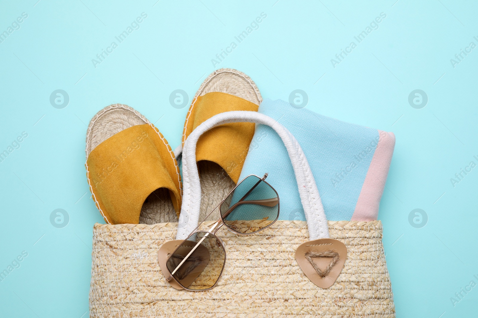 Photo of Wicker bag with beach objects on light blue background, flat lay