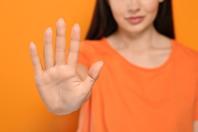 Photo of Woman showing stop gesture on orange background, selective focus