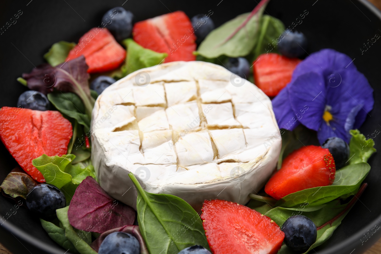 Photo of Delicious salad with brie cheese, blueberries and strawberries in bowl, closeup