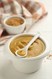 Photo of Bowl and spoon with tasty mustard sauce on white wooden table, closeup