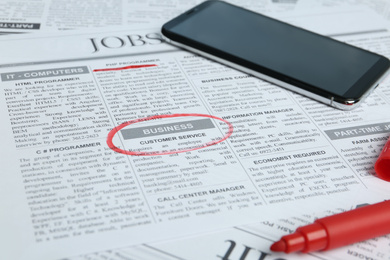 Newspaper with marked advertisement and smartphone. Job search concept