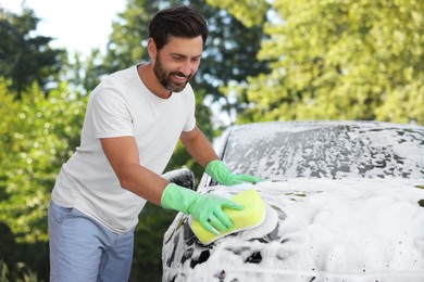 Photo of Happy man washing car with sponge outdoors