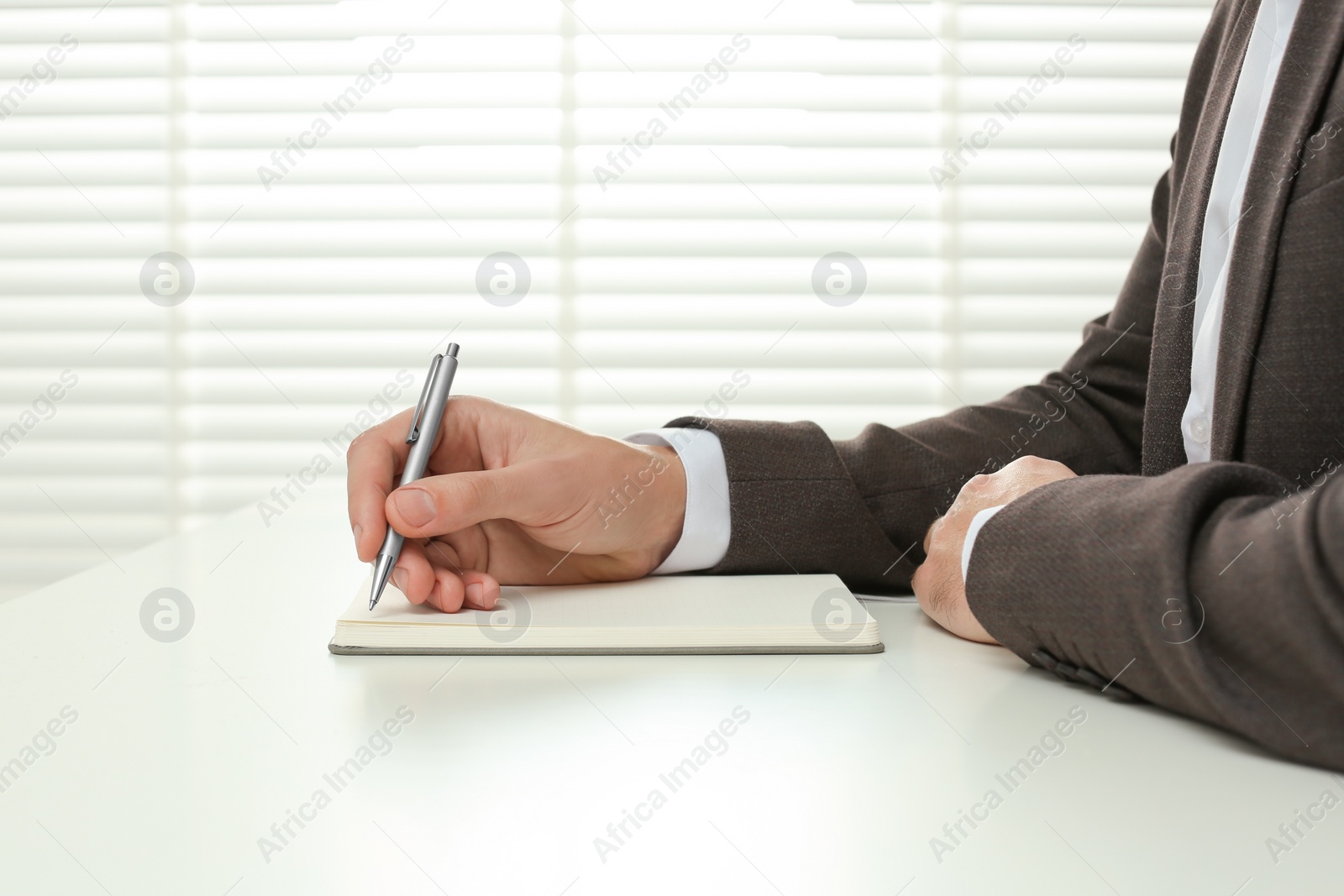 Photo of Man writing in notebook at white table indoors, closeup