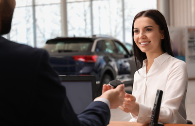 Photo of Salesman giving key to client in car dealership