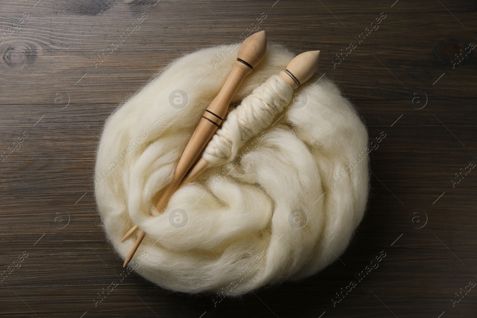 Photo of Soft white wool and spindles on wooden table, flat lay