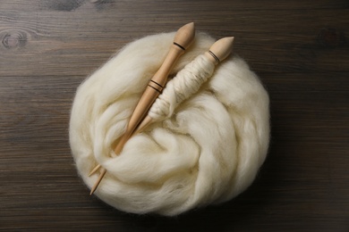 Photo of Soft white wool and spindles on wooden table, flat lay