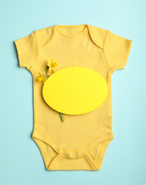 Photo of Child's bodysuit, flowers and card with space for text on light blue background, top view