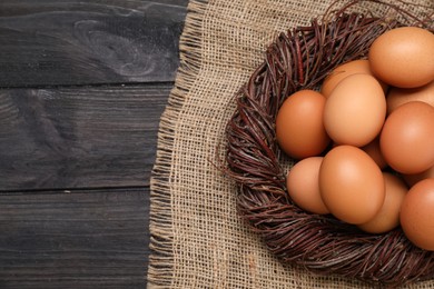 Fresh chicken eggs in nest on black wooden table, top view. Space for text