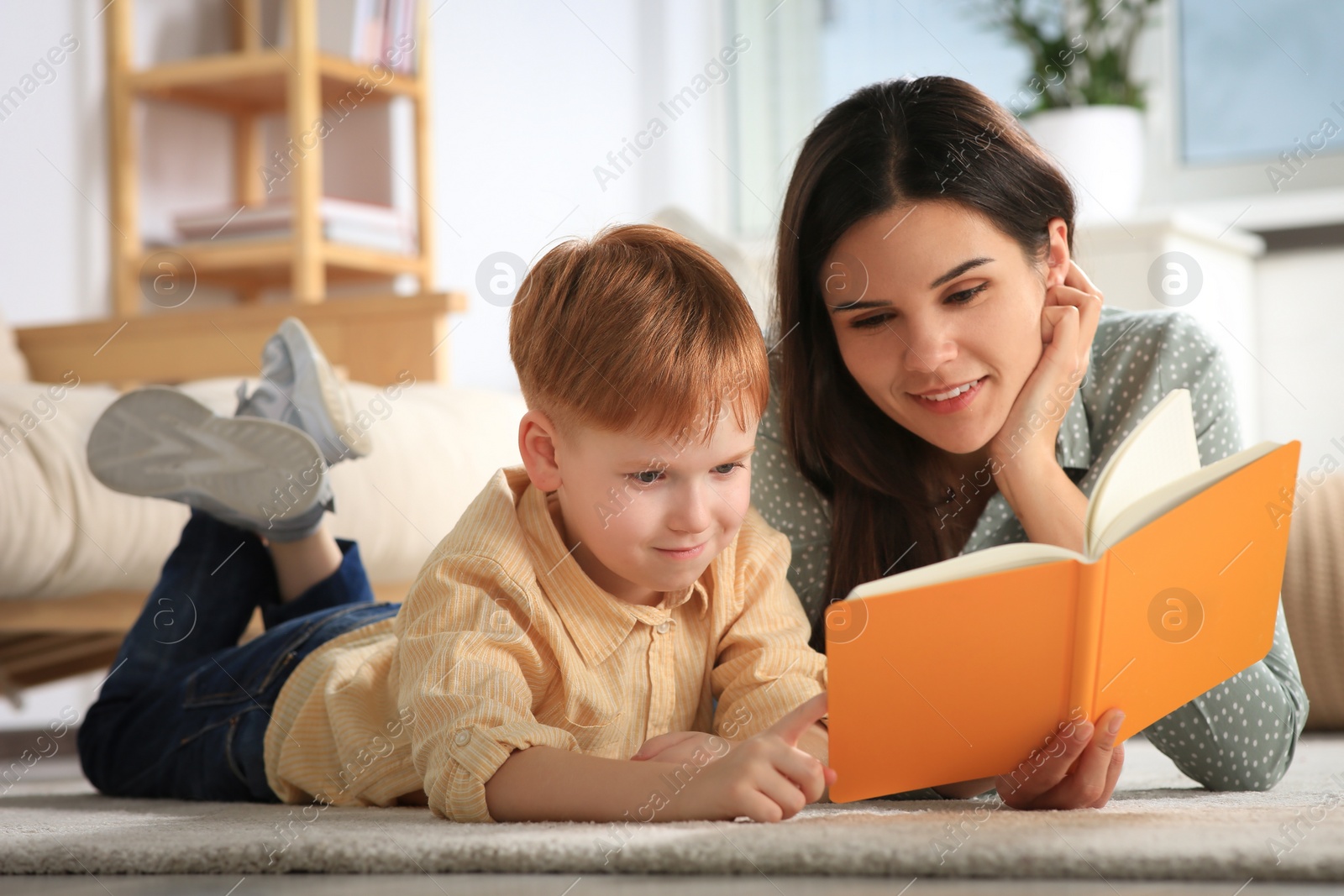 Photo of Mother reading book with her son on floor in living room at home