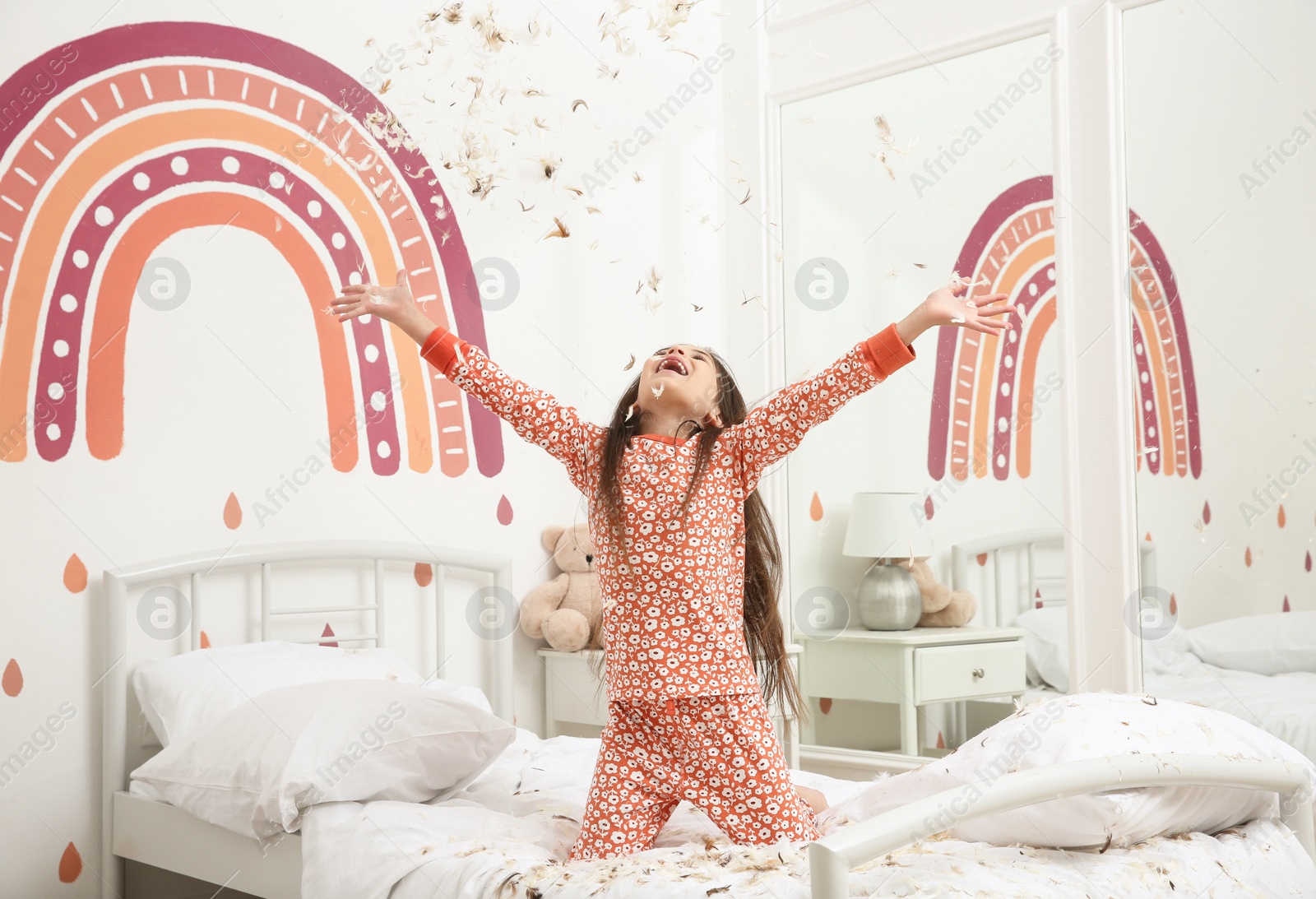 Photo of Cute little girl in pajamas playing with feathers on bed at home. Happy childhood