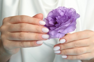 Photo of Woman with white nail polish holding violet eustoma flower, closeup
