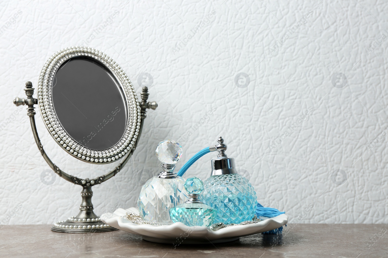 Photo of Plate with perfume bottles and jewellery near mirror on dressing table. Space for text