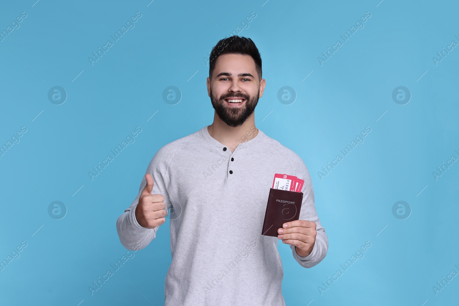 Photo of Smiling man with passport and tickets showing thumb up on light blue background