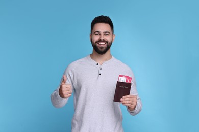 Smiling man with passport and tickets showing thumb up on light blue background