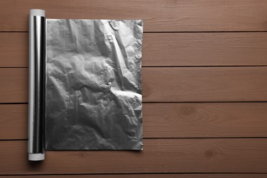 Roll of aluminum foil on wooden table, top view. Space for text