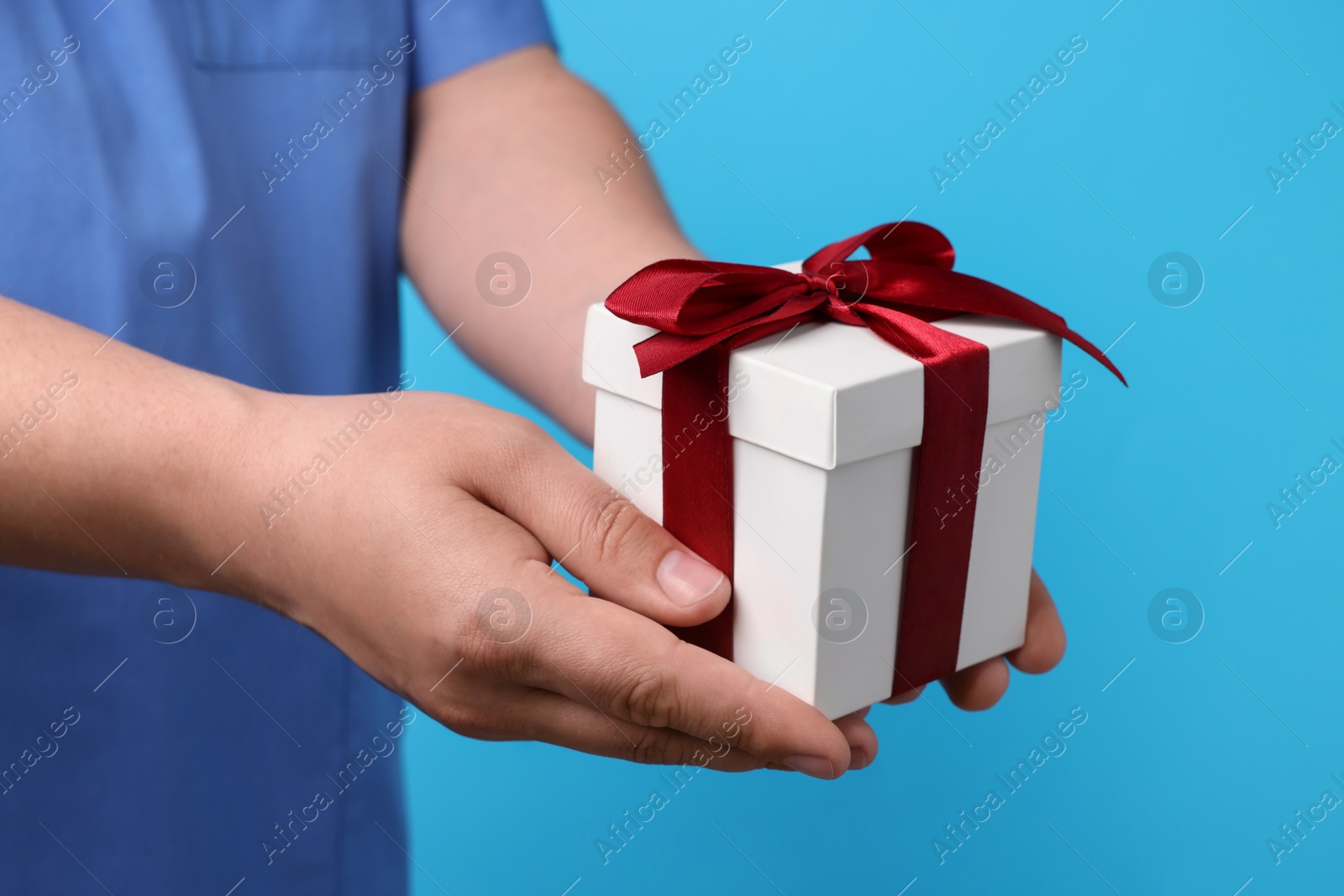 Photo of Doctor holding gift box on light blue background, closeup. Medical present