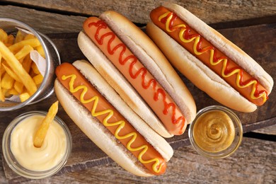 Delicious hot dogs with sauces and French fries on wooden table, top view