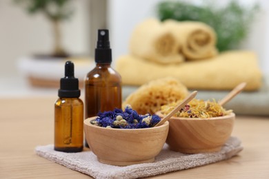 Bottles of essential oils, bowls with dry flowers and natural sponge on light wooden table, closeup. Spa therapy